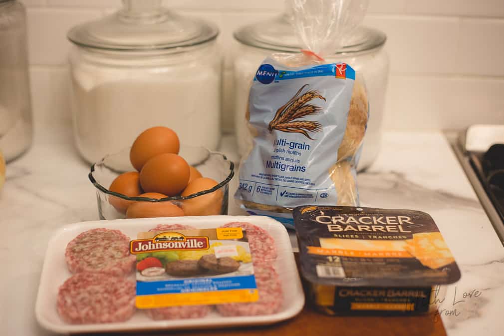 brown eggs in clear bowl, with bag of english muffins, package of uncooked pork, and cheese slices on a kitchen counter