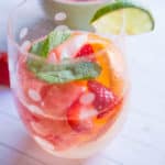 a glass filled with fresh fruit and white wine sangria, garnished with a lime slice