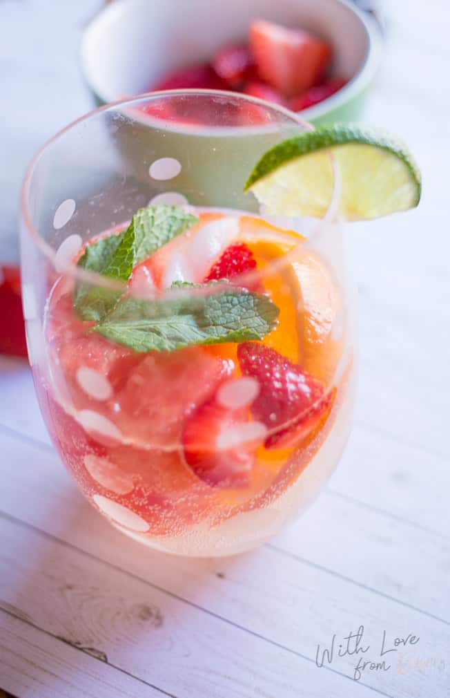 a glass filled with fresh fruit and white wine sangria, garnished with a lime slice