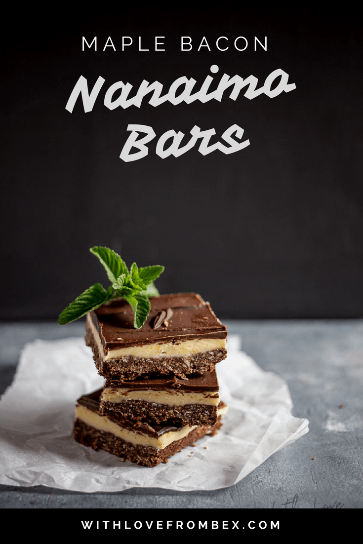 three maple bacon nanaimo bars stacked on top of each other topped with a mint leave against a black and gray background