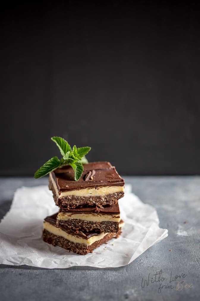 three maple bacon nanaimo bars stacked on top of each other topped with a mint leave against a black and gray background