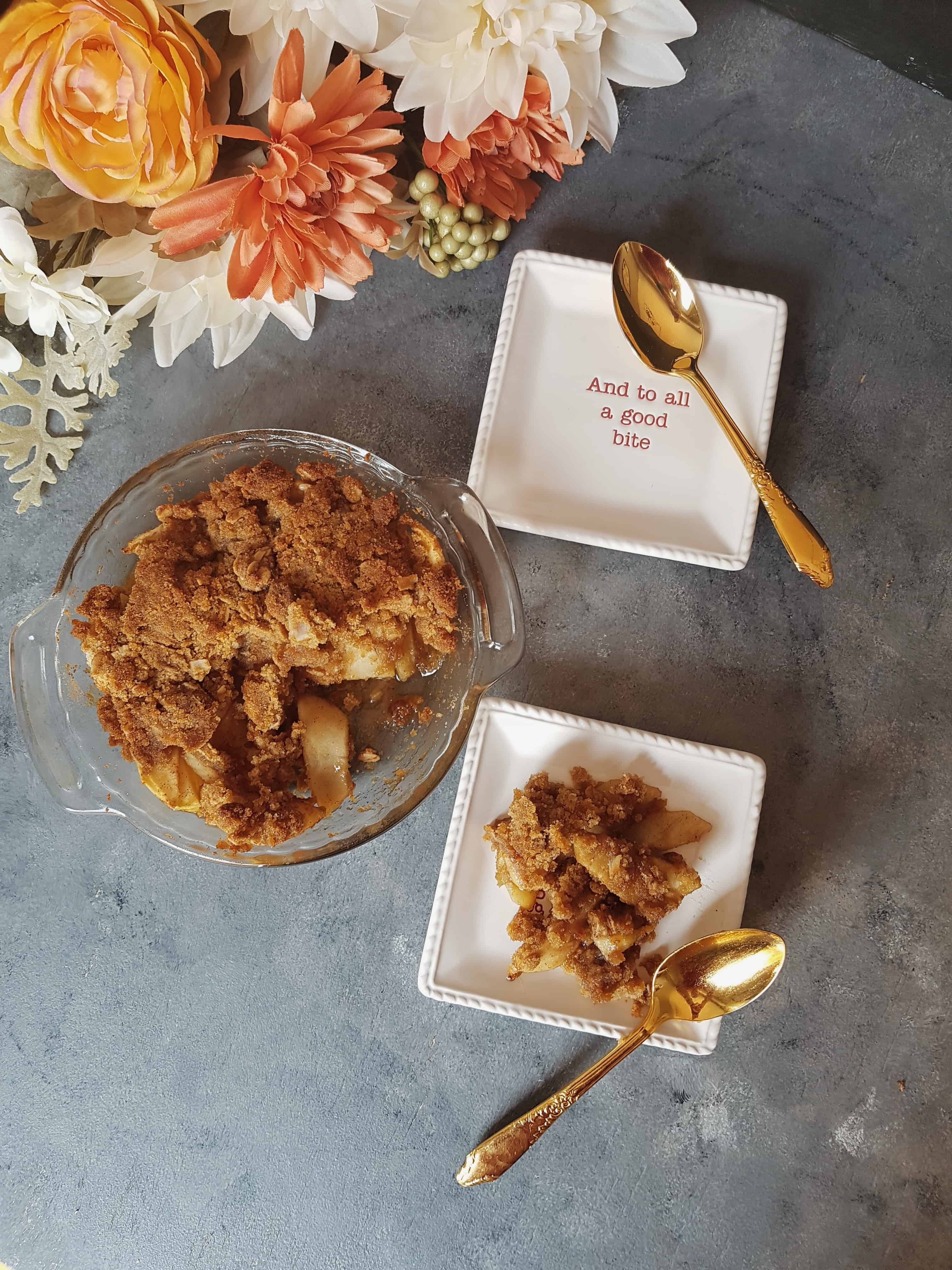 gluten free apple crisp in glass container with two white plates and gold spoons