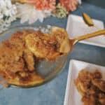 gold spoon with gluten free apple crisp on it, with two white plates and pan of apple crisp in background