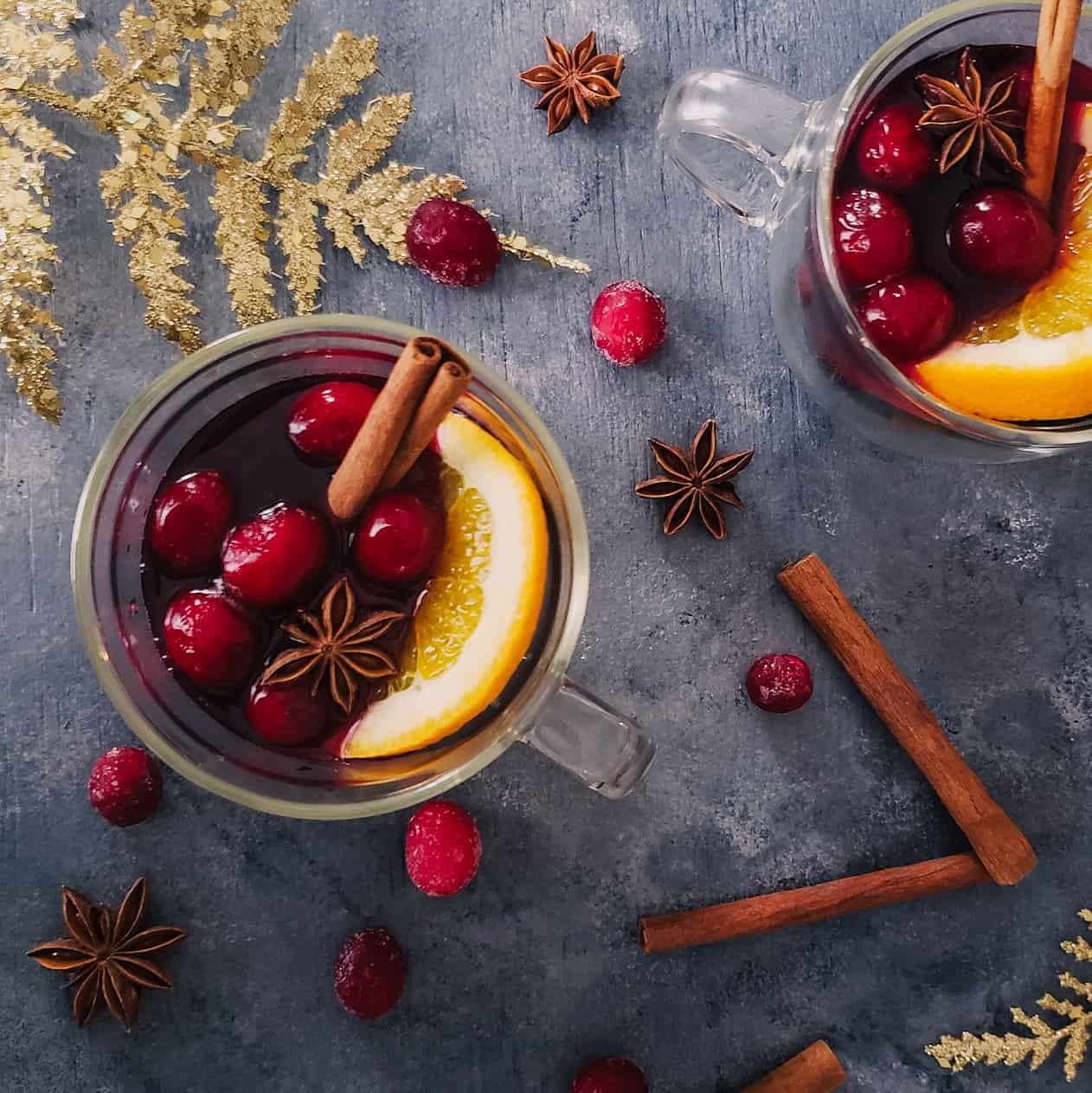 Two clear glasses of mulled red wine with cranberries and a slice of orange 