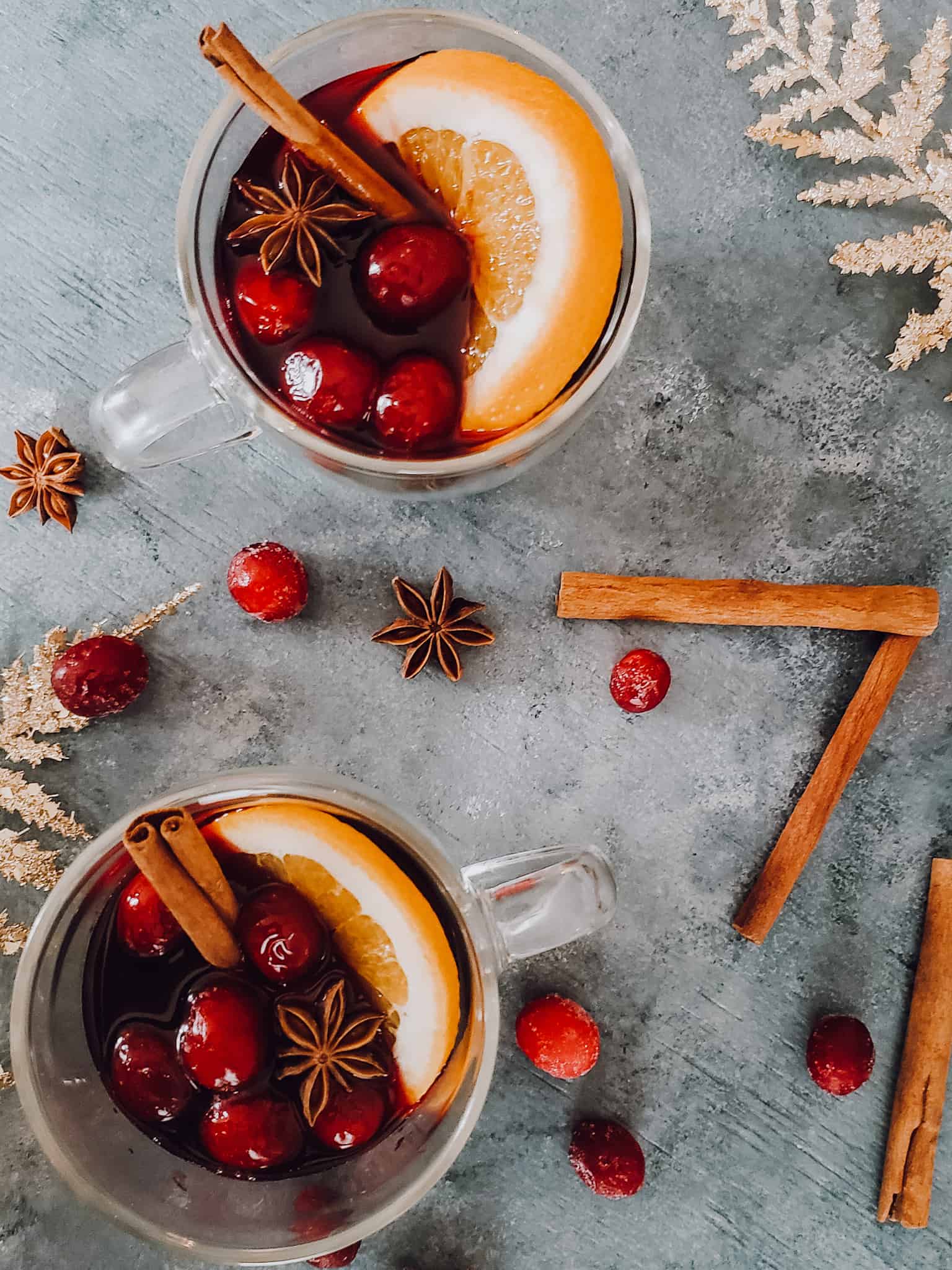 Two clear glasses of mulled red wine with cranberries and a slice of orange